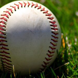 A baseball sitting in the grass with red laces.