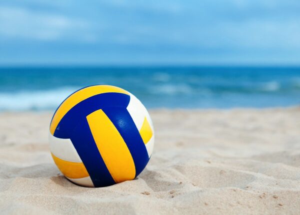 A beach volleyball ball on the sand near water.