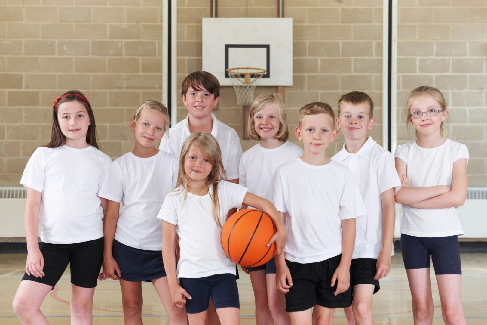 A group of children in white shirts holding a basketball.