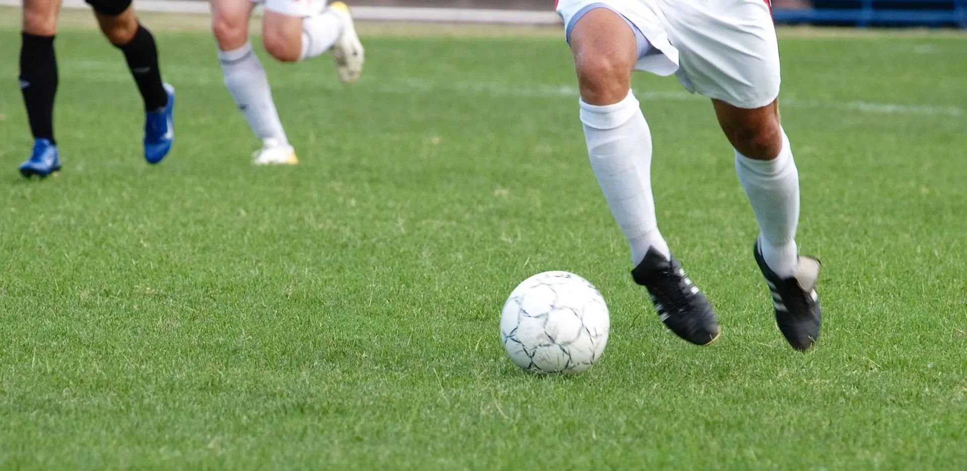 A soccer ball is on the ground with two players in front of it.