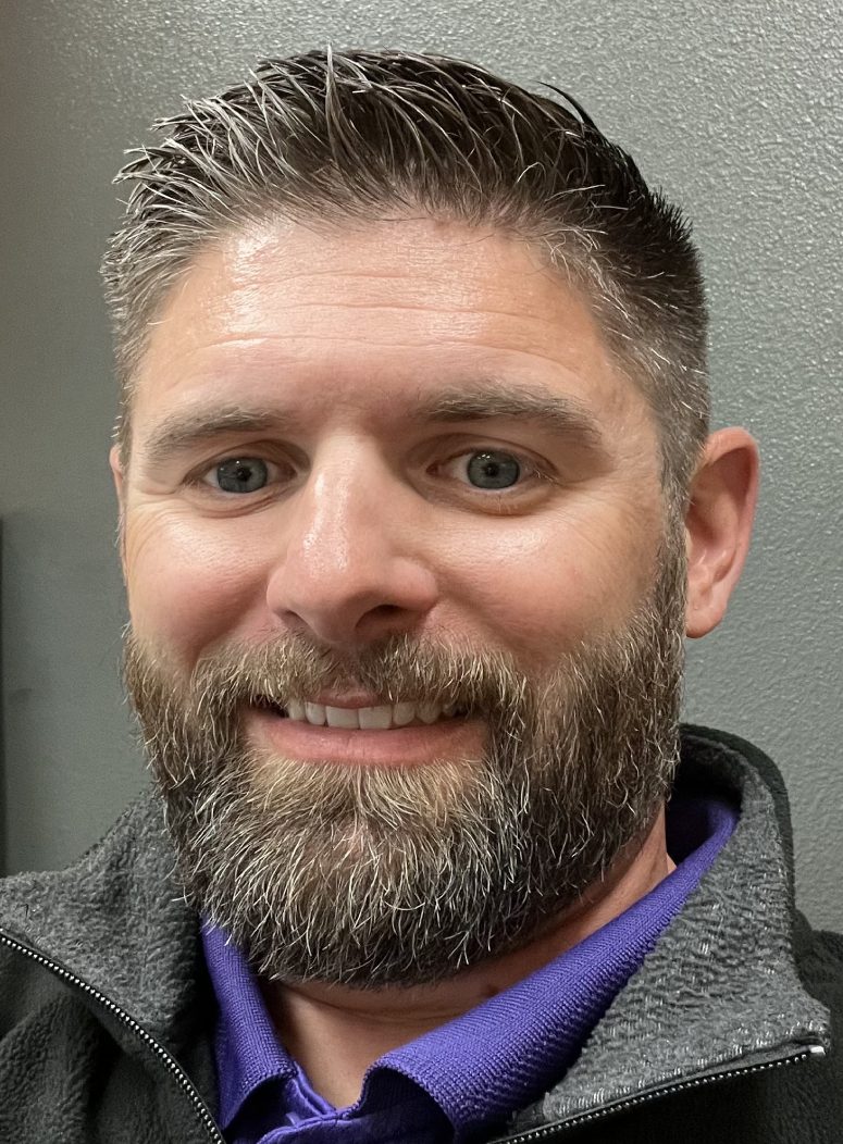 A man with a beard and mustache smiling for the camera.